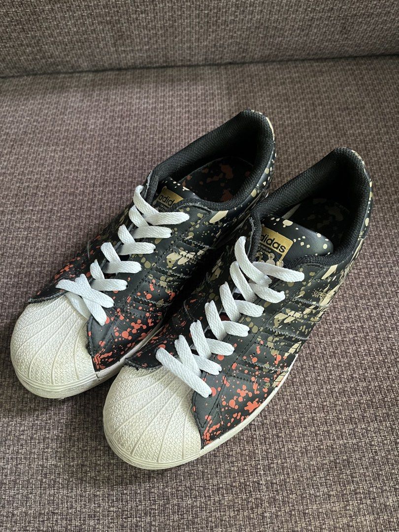 Adidas Superstar Camo Splatter Sneakers (Category: Sneakers) located in Manila. Submitted by lowkeyxan (Listing ID 1459985728, Image 2). Description: Original, Adidas Superstar sneakers with a black base, featuring a cool camo splatter design in orange and gold. Classic shell toe and white laces. Perfect for everyday style. .