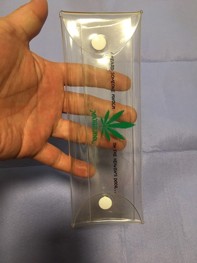 Clear Pencil Case with Marijuana Leaf Design (Category: Stationery & School Supplies) located in Pasay City. Submitted by gilbertso62551 (Listing ID 1460048240, Image 2). Description: - Clear plastic pencil case - Features a green marijuana leaf graphic - Text reads 'I HEARD SOMEONE KNOCK ON THE HEAVEN'S DOOR... MARIJUANA' - Two white snap closures for secure storage - Ideal for pens, pencils, and other small items - Approximately 8 inches long -
