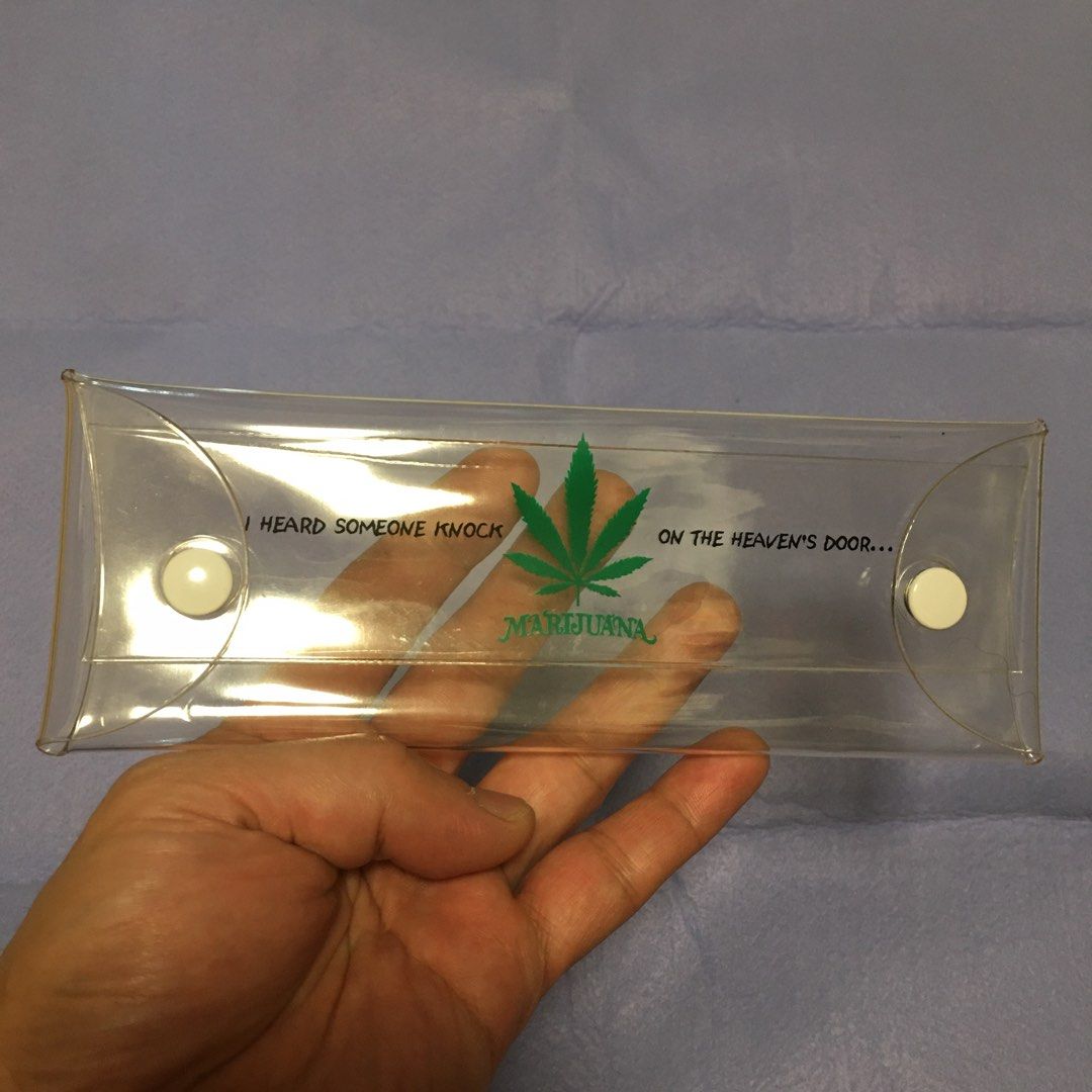Clear Pencil Case with Marijuana Leaf Design (Category: Stationery & School Supplies) located in Pasay City. Submitted by gilbertso62551 (Listing ID 1460048240, Image 1). Description: - Clear plastic pencil case - Features a green marijuana leaf graphic - Text reads 'I HEARD SOMEONE KNOCK ON THE HEAVEN'S DOOR... MARIJUANA' - Two white snap closures for secure storage - Ideal for pens, pencils, and other small items - Approximately 8 inches long -