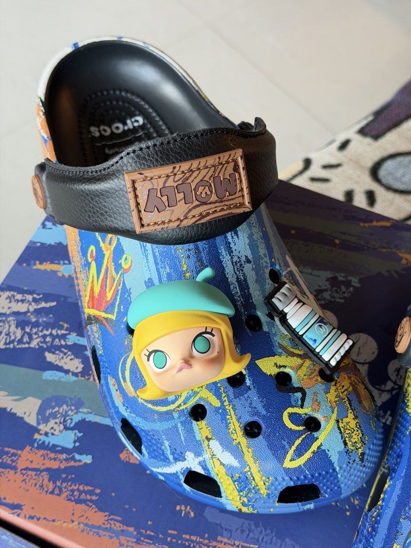 Crocs x Pop Mart Molly Artist Collection Clogs (Category: Slippers and slides) located in Taguig. Submitted by Yukandfriends (Listing ID 1459994222, Image 3). Description: - Authentic Crocs x Pop Mart Molly collaboration clogs. - Features an artist theme with unique paint tube and palette Jibbitz. - Stylish blue base with an abstract paint splatter design. - Comes complete with the original box. - A must-have for collectors and fans of Molly and 