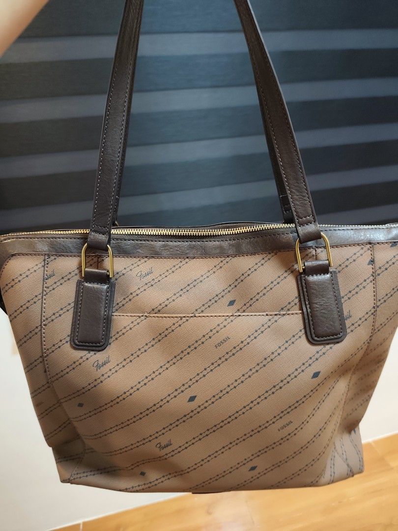 Fossil Brown Monogram Tote Bag with Stripes (Category: Tote Bags) located in Santo Tomas. Submitted by prelovedthrifts (Listing ID 1460019435, Image 3). Description: - Authentic brown Fossil tote bag - All-over signature Fossil monogram pattern - Three vertical stripes (brown & cream) on the front - Genuine leather handles and trim - Secure zipper closure - Multiple interior pockets for organization - Comes with a detachable Fossil key charm This