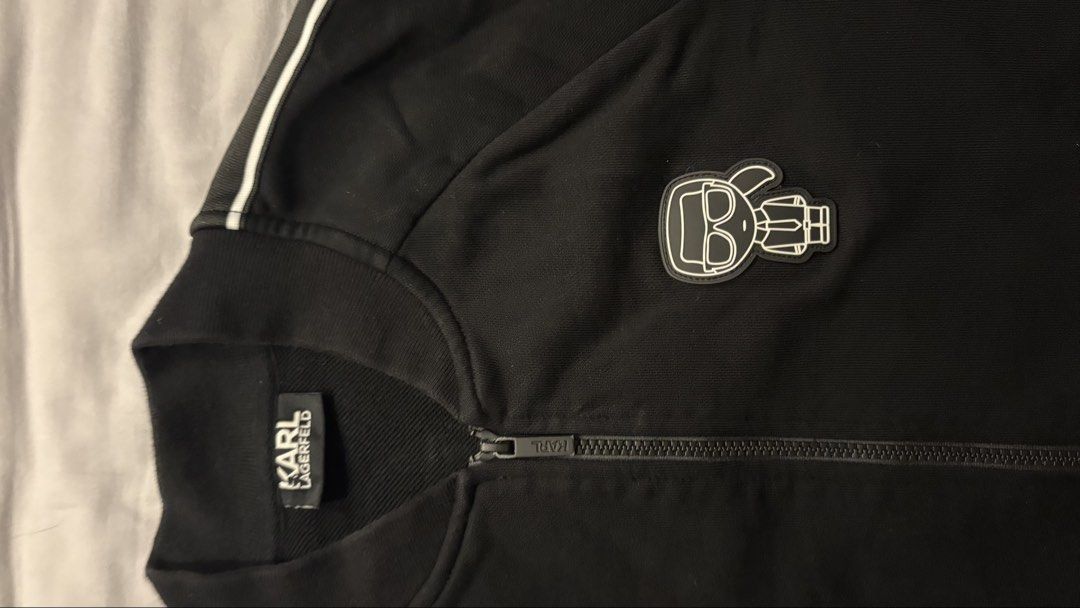 Karl Lagerfeld Black Track Jacket with Logo (Category: Coats, Jackets and Outerwear) located in Dasmarinas. Submitted by stephen08e (Listing ID 1460026297, Image 2). Description: - Authentic Karl Lagerfeld black track jacket - Features iconic Karl Lagerfeld character logo on chest - White stripe detailing with repeating brand name on sleeves - Full zip front closure - Convenient side pockets.
