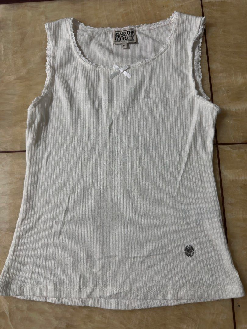Marithe Francois Girbaud White Ribbed Tank Top Size S (Category: Sleeveless) located in Manila. Submitted by jessj30 (Listing ID 1460002276, Image 2). Description: - White ribbed tank top by Marithe Francois Girbaud - Features a small bow detail at the neckline - Subtle logo emblem on the front - Sleeveless design - Scalloped hem - Made from a comfortable cotton blend - Ideal basic piece for everyday outfits.