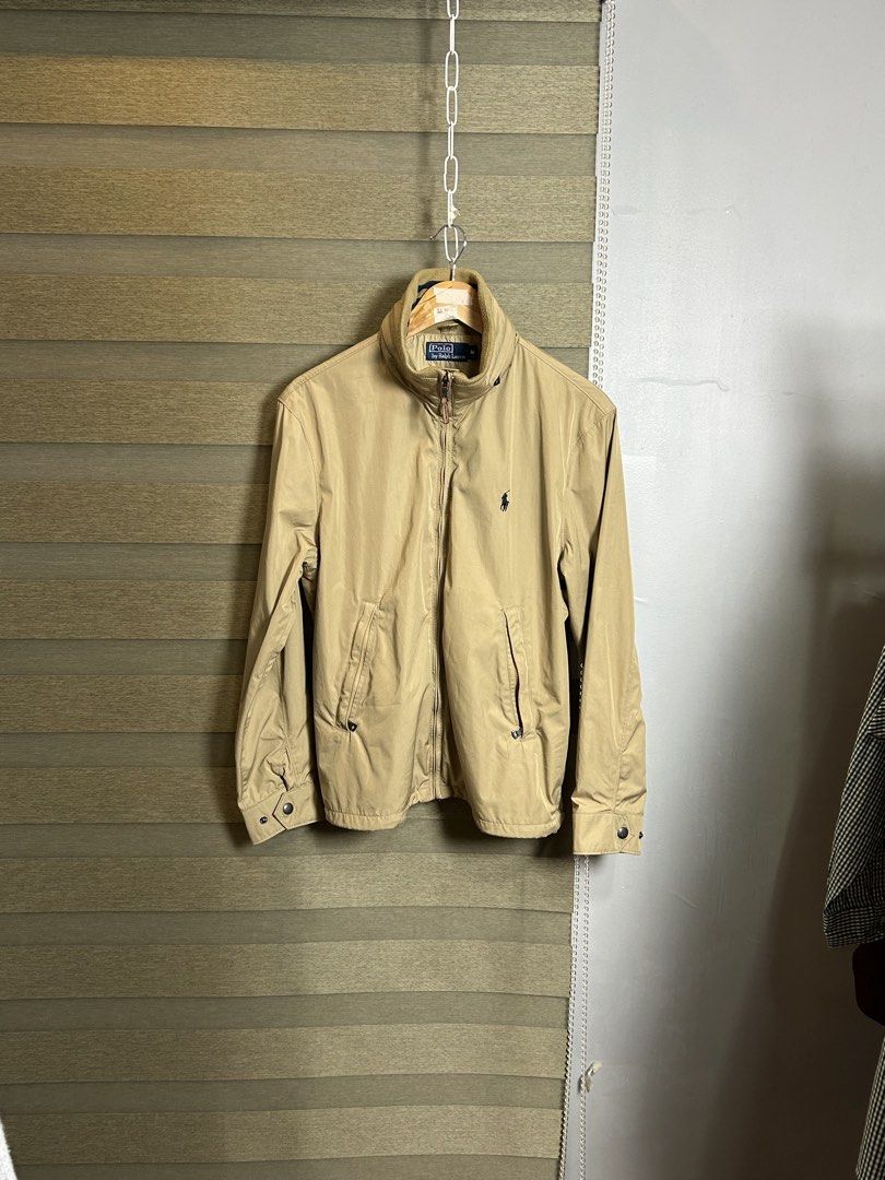 Polo Ralph Lauren Khaki yatch Jacket (Category: Coats, Jackets and Outerwear) located in Santa Ana. Submitted by thrift.sanctuary (Listing ID 1460051782, Image 1). Description: Classic khaki jacket from Polo Ralph Lauren. Features the iconic polo player logo embroidered on the chest. Zip-up front with a leather pull tab. Two front pockets with button closures. Striped detail on the inner collar. Great for layering..