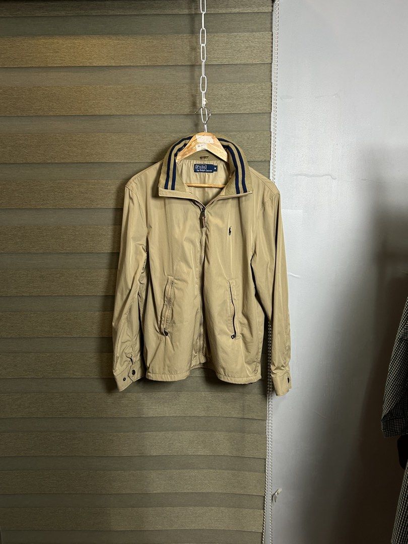 Polo Ralph Lauren Khaki yatch Jacket (Category: Coats, Jackets and Outerwear) located in Santa Ana. Submitted by thrift.sanctuary (Listing ID 1460051782, Image 2). Description: Classic khaki jacket from Polo Ralph Lauren. Features the iconic polo player logo embroidered on the chest. Zip-up front with a leather pull tab. Two front pockets with button closures. Striped detail on the inner collar. Great for layering..
