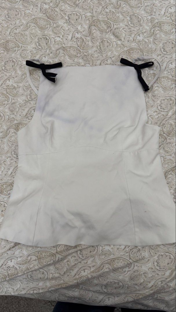White Halter Neck Top with Black Bows (Category: Sleeveless) located in Makati City. Submitted by shaniahdeclutters (Listing ID 1459968297, Image 1). Description: - HAS STAINS - White halter neck top - Features cute black bows on the straps - Fitted waist for a flattering silhouette - Perfect for dressing up or down.