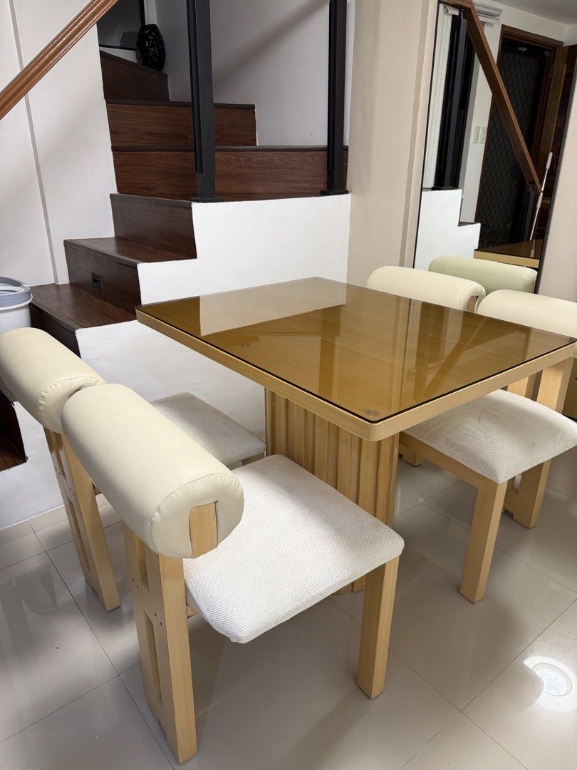 4-Seater Dining Set (Category: Tables & Sets) located in Rodriguez. Submitted by itschristinemunoz (Listing ID 1460198273, Image 1). Description: - Square glass top dining table - Sturdy wooden base - Includes 4 upholstered chairs - Chairs feature light-colored fabric seats - Cream-colored padded backrests - Ideal for small dining areas or kitchens - Ready for a new home.