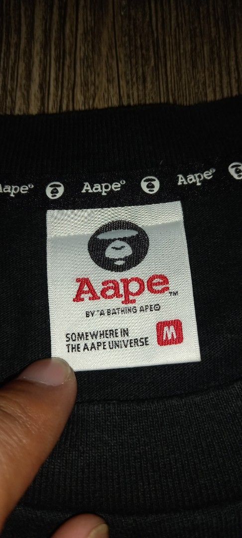AAPE BY A BATHING APE (Category: Tshirts & Polo Shirts ) located in Cavite. Submitted by chard112345 (Listing ID 1460158269, Image 3). Description: - Brand: AAPE BY A BATHING APE - Color: Black - Size: L to Xl - Material: 100% Cotton - Front Design: AAPE logo and planet graphic - Back Design: Text reads 'SOMEWHERE IN THE AAPE UNIVERSE BY A BATHING APE'.
