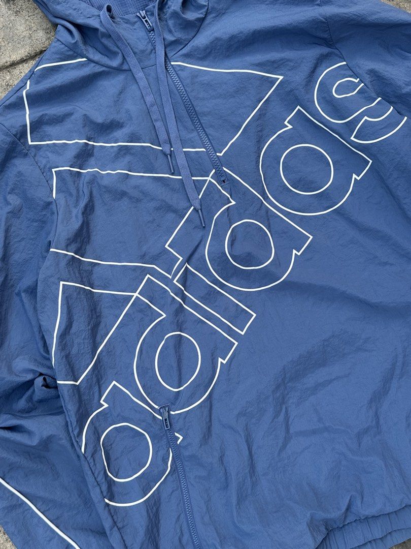 Adidas Blue Windbreaker Jacket with Large Logo (Category: Coats, Jackets and Outerwear) located in Padada. Submitted by jevanie1234 (Listing ID 1460269417, Image 2). Description: - Blue Adidas windbreaker jacket - Size: A/2XL - Features a hood and zip closure - Two zip pockets on the front - Large white Adidas logo across the front - Mesh lining inside - Made in Indonesia.