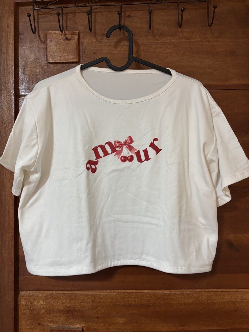 'Amour' Cherry Graphic Cropped T-shirt (Category: Shirts) located in Trece Martires City. Submitted by decluttercloset_niks (Listing ID 1460298603, Image 1). Description: - White cropped t-shirt - Features a cute red 'Amour' graphic with cherries and a bow - Short sleeves - Relaxed fit - Ideal for casual wear - Pairs well with jeans or skirts.