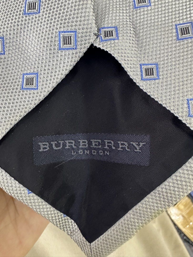 Burberry London Silk Tie (Category: Ties) located in Manila. Submitted by declutterpromax (Listing ID 1460195377, Image 3). Description: - Classic Burberry tie - 100% Silk - Subtle blue and black geometric pattern on light grey background - Small stain on the front (please check photos) - Ideal for formal occasions or adding luxury to your outfit.