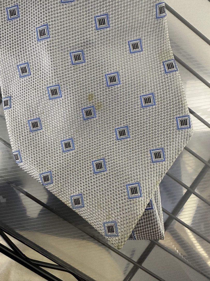 Burberry London Silk Tie (Category: Ties) located in Manila. Submitted by declutterpromax (Listing ID 1460195377, Image 2). Description: - Classic Burberry tie - 100% Silk - Subtle blue and black geometric pattern on light grey background - Small stain on the front (please check photos) - Ideal for formal occasions or adding luxury to your outfit.