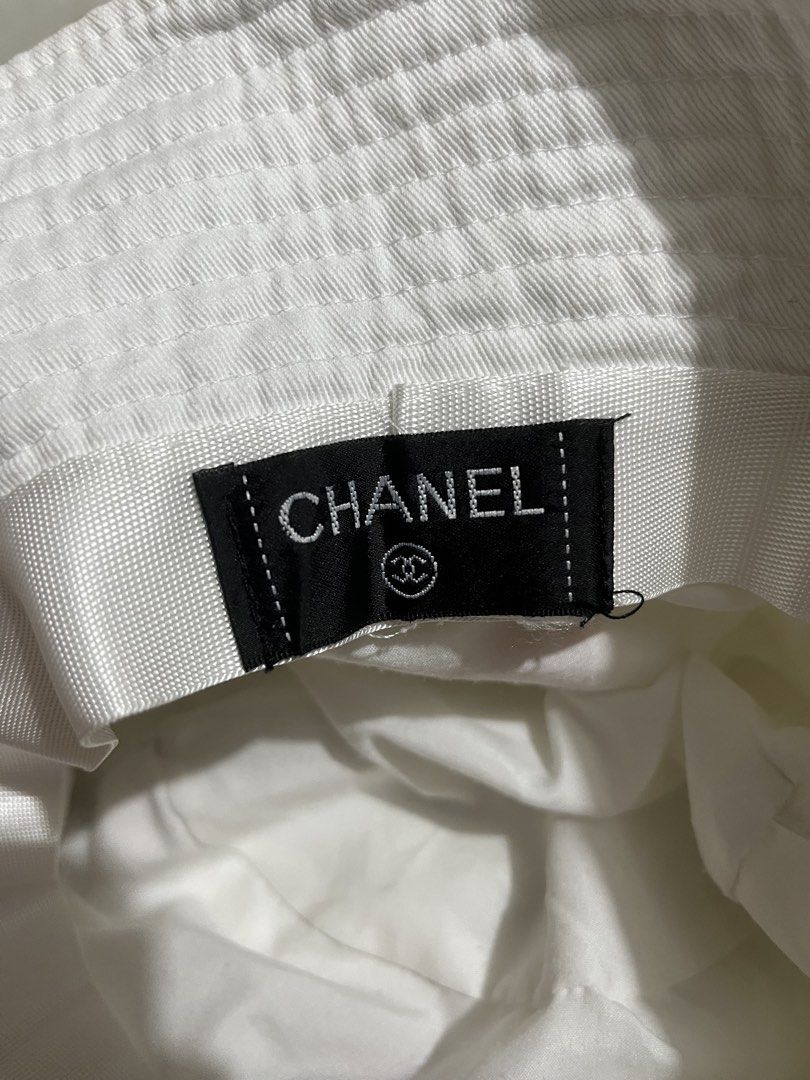 Chanel x Pharrell Williams White Bucket Hat (Category: Hats & Beanies) located in Pilar. Submitted by fast-flip-ni-miko. (Listing ID 1460274932, Image 3). Description: - White bucket hat - Red 'Chanel Pharrell' embroidery on one side - Iconic CC logo with rainbow stripes on the other side - Classic Chanel tag inside - Ideal for sunny days - A cool accessory to elevate any outfit.