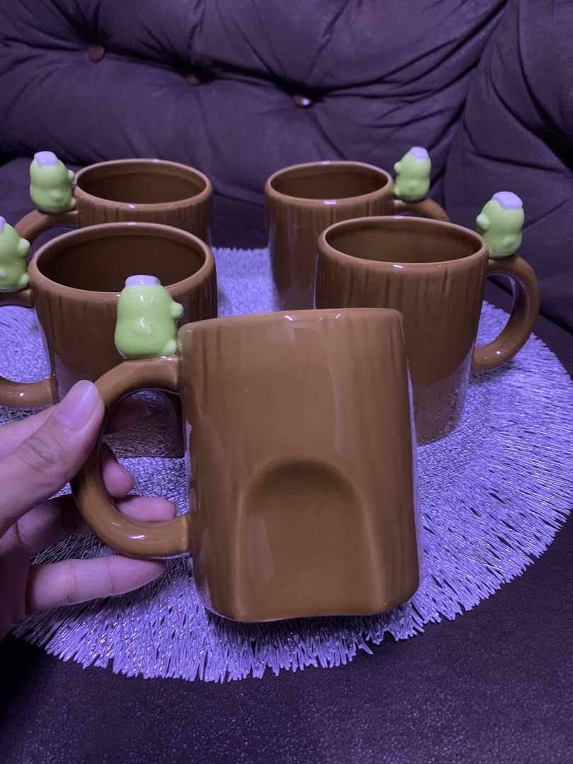 Cute Frog Ceramic Mugs Set of 4 (Category: Coffee & Tea Tableware) located in Cavite. Submitted by thinkerbelle_certified (Listing ID 1460216983, Image 1). Description: - Set of 4 brown ceramic mugs - Each mug features a cute green frog on the handle - Unique textured design resembling tree bark - Ideal for coffee, tea, or hot chocolate - Makes a great gift or a fun kitchen addition.