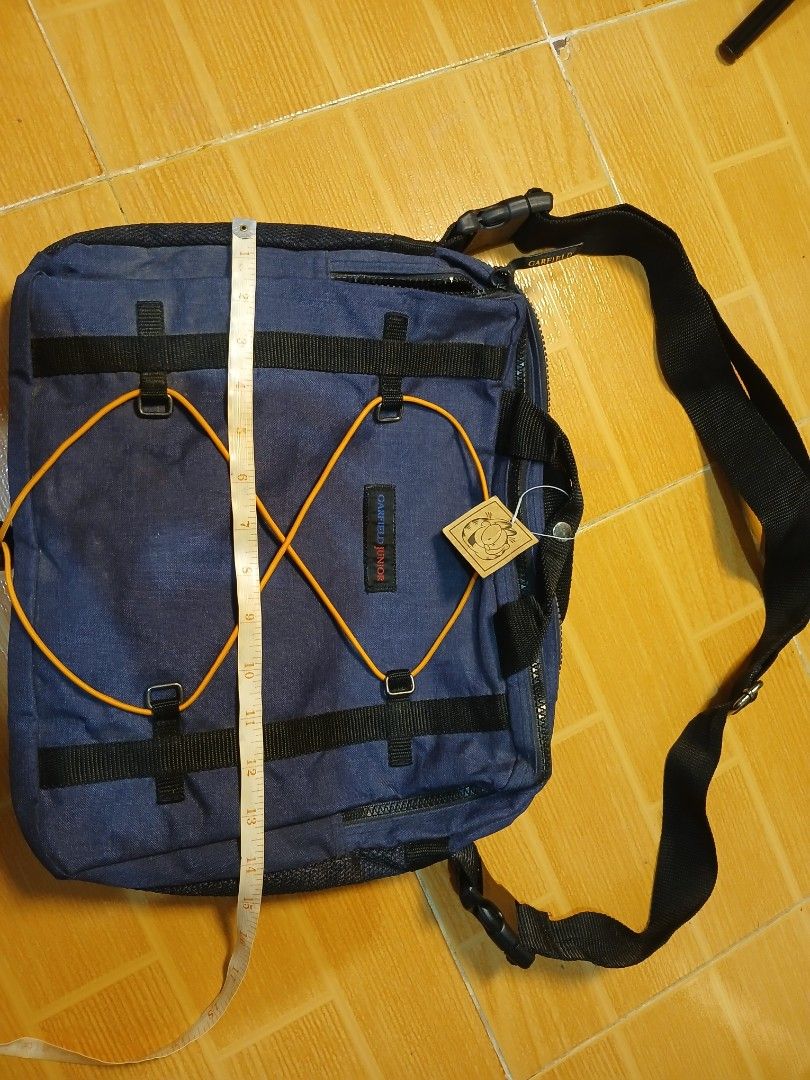 Garfield Juniors Navy Blue Messenger Bag (Category: Sling Bags) located in Manila. Submitted by asianwave189184 (Listing ID 1460247201, Image 1). Description: - Navy blue messenger bag from Garfield Juniors - Adjustable strap with buckle closure - Unique bungee cord detail on the front - Multiple pockets and compartments for organization - Ideal for school or everyday carry - Approximately 14 inches wide.