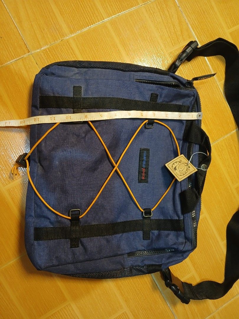 Garfield Juniors Navy Blue Messenger Bag (Category: Sling Bags) located in Manila. Submitted by asianwave189184 (Listing ID 1460247201, Image 2). Description: - Navy blue messenger bag from Garfield Juniors - Adjustable strap with buckle closure - Unique bungee cord detail on the front - Multiple pockets and compartments for organization - Ideal for school or everyday carry - Approximately 14 inches wide.