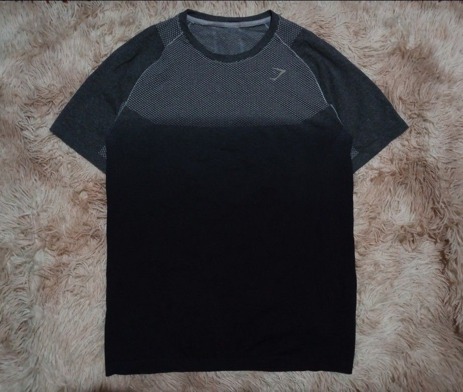 Gymshark Seamless T-shirt (Category: Activewear) located in Boston. Submitted by johnpaulvi30029 (Listing ID 1460242385, Image 1). Description: - Gymshark seamless t-shirt - Color: Dark grey and black gradient - Features breathable knit pattern on chest and back - Short sleeves - Ideal for workouts or casual wear - Comfortable and lightweight material.