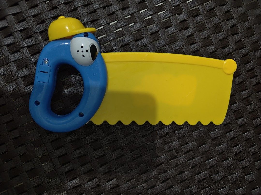 Handy Tools Toy Saw with Funny Face (Category: Kids Toys) located in Mandaluyong City. Submitted by declutterpreloved2.0 (Listing ID 1460269252, Image 2). Description: - Cute yellow toy saw with a blue handle and funny face. - Features a yellow hard hat on its head. - 'Handy Tools' is written on the saw blade. - Perfect for pretend play and imaginative building adventures. - Potential electronic features on the handle (functionality not guarantee