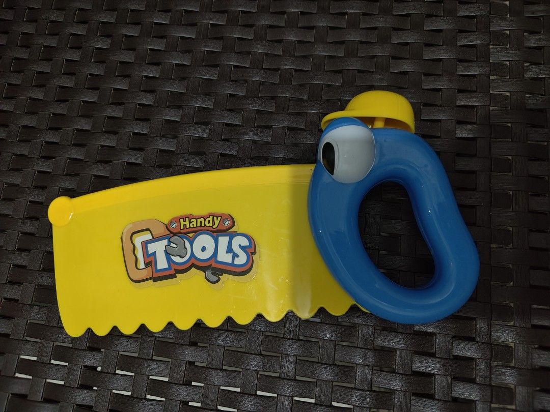 Handy Tools Toy Saw with Funny Face (Category: Kids Toys) located in Mandaluyong City. Submitted by declutterpreloved2.0 (Listing ID 1460269252, Image 1). Description: - Cute yellow toy saw with a blue handle and funny face. - Features a yellow hard hat on its head. - 'Handy Tools' is written on the saw blade. - Perfect for pretend play and imaginative building adventures. - Potential electronic features on the handle (functionality not guarantee