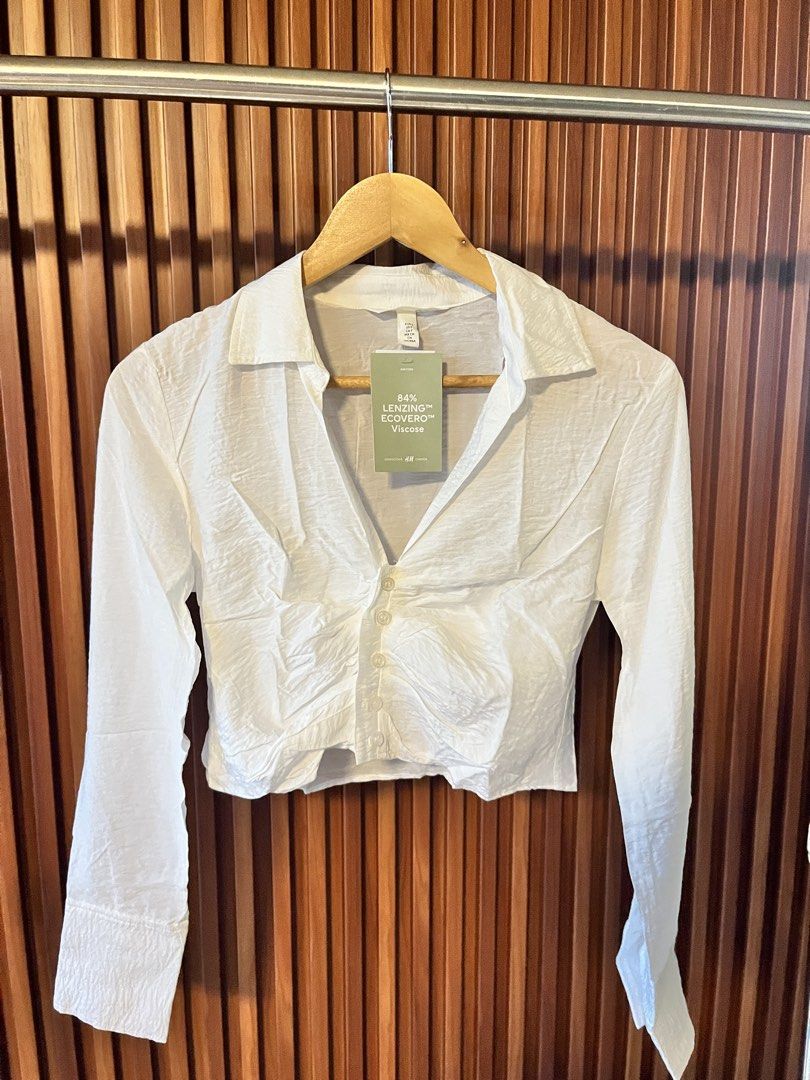 H&M White Cropped Shirt with Collar (Category: Shirts) located in Echague. Submitted by aeafitz (Listing ID 1460304792, Image 1). Description: - White cropped shirt from H&M - Made with 84% LENZING™ ECOVERO™ Viscose (eco-friendly material) - Collared neckline - Button-up front - Long sleeves with buttoned cuffs - Textured fabric - Versatile for layering or wearing solo.