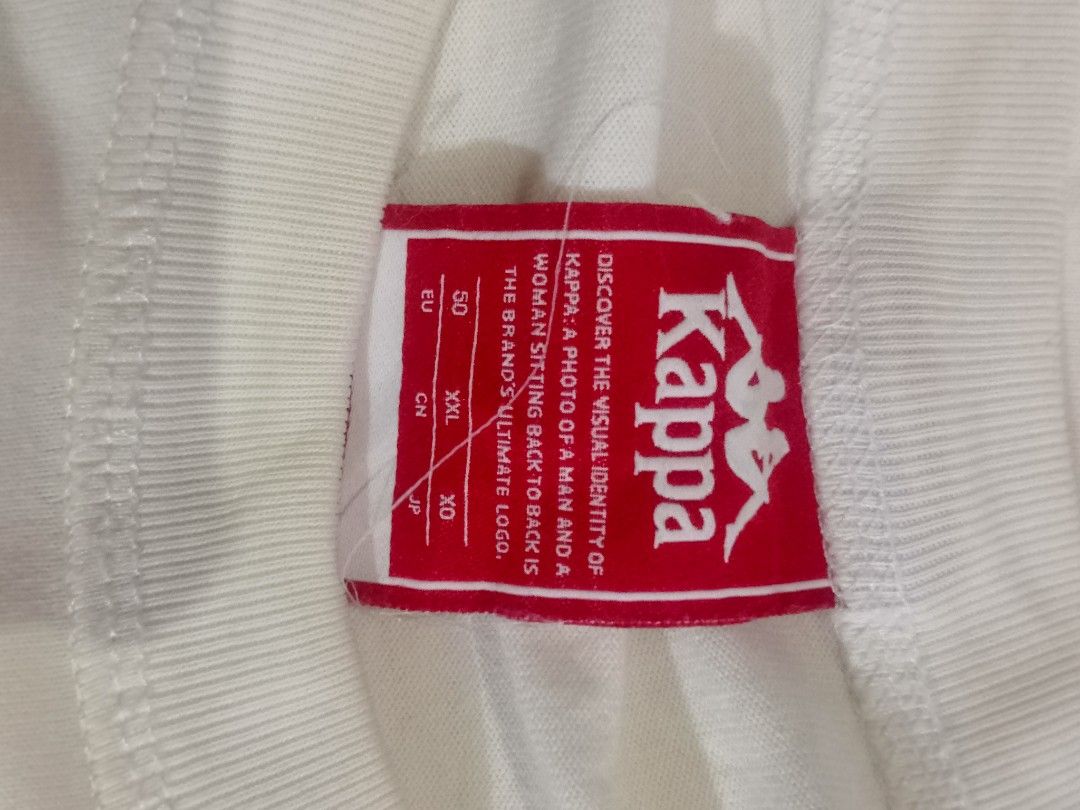 Kappa White T-Shirt (Category: Tshirts & Polo Shirts ) located in Oas. Submitted by yortzzz (Listing ID 1460275099, Image 3). Description: - White Kappa T-shirt - Size: XXL - Features oval logo and 'SPORTWEAR BRAND LIKE NO OTHER' text graphic - Small Kappa logo patch on bottom left - Material: Cotton blend.