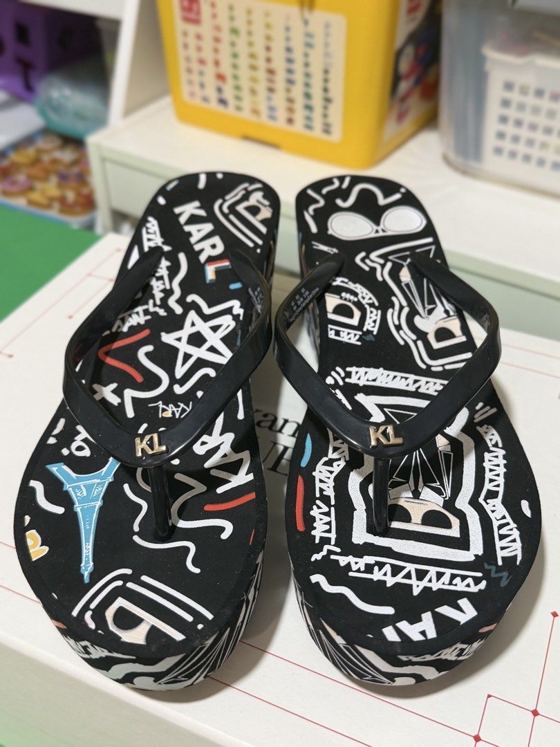 Karl Lagerfeld Black Graffiti Wedge Flip Flops (Category: Slippers and slides) located in Marikina City. Submitted by sisbasco999 (Listing ID 1460290707, Image 1). Description: - Authentic Karl Lagerfeld wedge flip flops - Stylish black with a vibrant graffiti print - Features the iconic KL logo on the straps - Comfortable platform sole for a subtle lift - Ideal for beach days or everyday casual wear - Unique and eye-catching design.