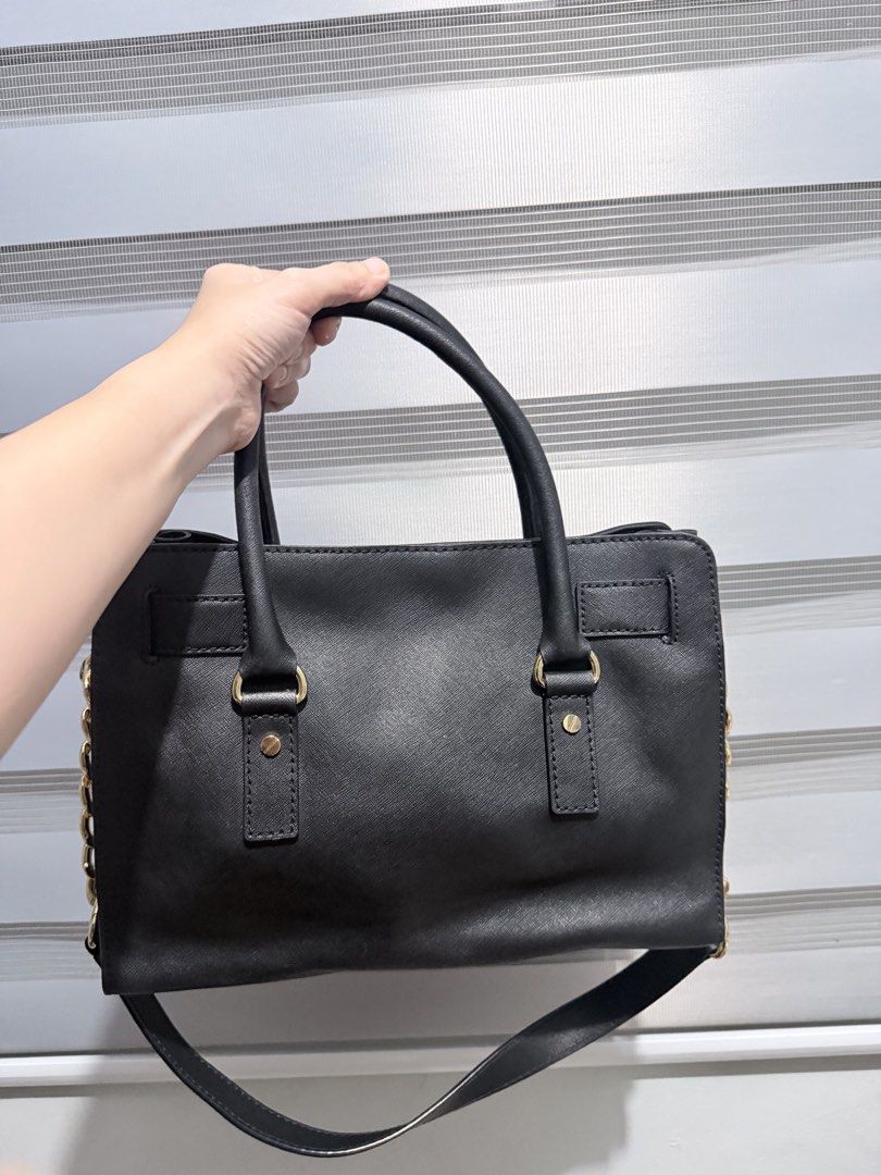 Michael Kors Hamilton Satchel Saffiano Leather (Category: Shoulder Bags) located in Manila. Submitted by prelovedbygayle (Listing ID 1460276079, Image 2). Description: Silhouette & Structure: Features a structured, trapezoidal tote silhouette with a belted top trim. Hardware: Accented with polished gold-tone hardware, including a prominent engraved “MK” logo padlock on the center front and attached decorative key clochette. Carrying Options: Outf