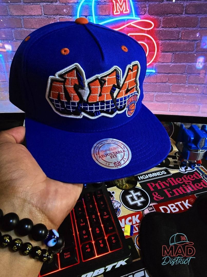 Mitchell & Ness New York Knicks Graffiti Snapback Cap (Category: Caps & Hats) located in Pasig City. Submitted by markyboi888 (Listing ID 1460190313, Image 1). Description: - Mitchell & Ness New York Knicks snapback cap - Features a bold graffiti-style logo on the front - Adjustable fit at the back - Color: Royal blue with orange and white accents - Perfect for any Knicks fan.