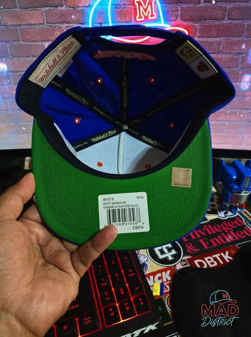 Mitchell & Ness New York Knicks Graffiti Snapback Cap (Category: Caps & Hats) located in Pasig City. Submitted by markyboi888 (Listing ID 1460190313, Image 3). Description: - Mitchell & Ness New York Knicks snapback cap - Features a bold graffiti-style logo on the front - Adjustable fit at the back - Color: Royal blue with orange and white accents - Perfect for any Knicks fan.