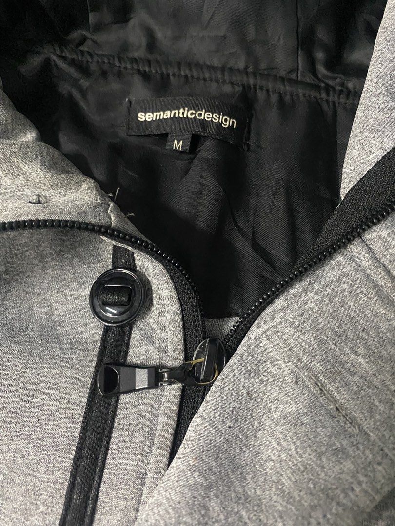 Semantic Design Grey Hooded Jacket Size M (Category: Coats, Jackets and Outerwear) located in Santa Maria. Submitted by saintarchive316 (Listing ID 1460252169, Image 2). Description: - Grey hooded jacket from Semantic Design - Size: Medium (M) - Features: Zip pocket on chest, button pockets on sides, drawstring hood - Material: Polyester blend - Ideal for: Casual wear.