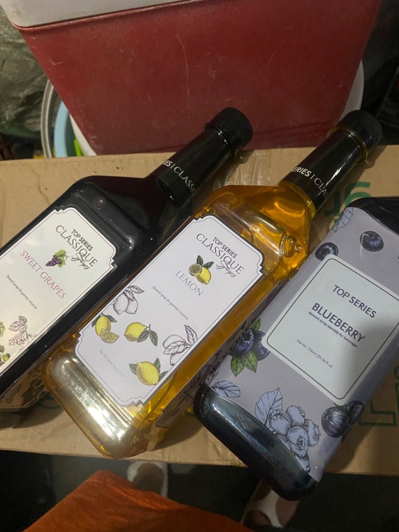 Top Series Syrups (Category: Beverages) located in San Fernando. Submitted by wise_meowcath (Listing ID 1460170721, Image 2). Description: - Brand: Top Series Classique - Flavors: Sweet Grapes, Lemon, Blueberry - Packaging: Stylish bottles with unique flavor-themed labels - Usage: Ideal for coffee, milk tea, cocktails, desserts, and other beverages - Quality: Premium syrups for enhanced flavor.