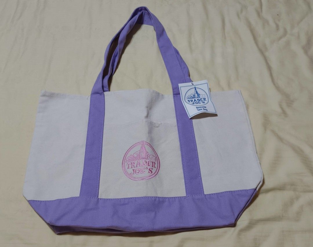 Trader Joe's (Category: Tote Bags) located in Tarlac. Submitted by allysarusanguieb_25 (Listing ID 1460302673, Image 1). Description: **Trader Joe's Canvas Tote Bag (Lavender / Purple)** **Listing Details** * **Item**: Trader Joe's Canvas Tote Bag * **Color**: White body with Lavender/Purple contrast trim, handles, and embroidered logo * **Condition**: Brand New with Tags Attached (NWT) **Key Features** * **100% Authentic**: Features original sto