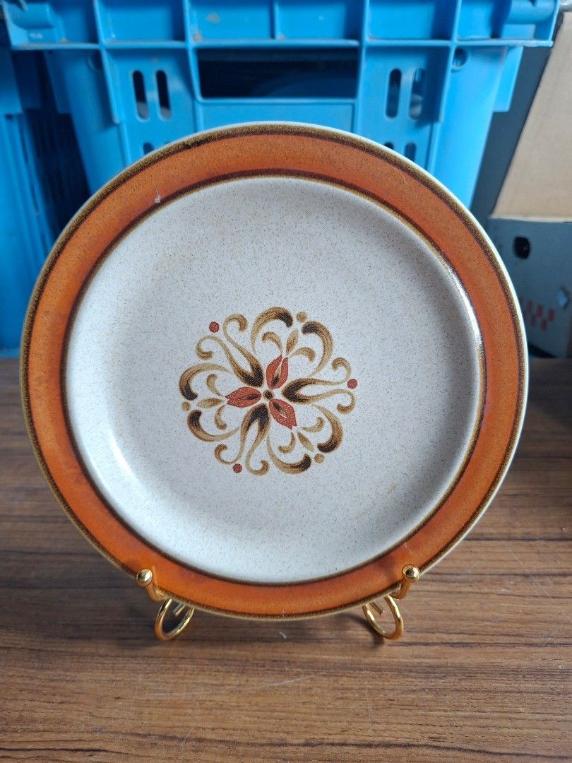1970s Arabesco Stoneware Plate (Category: Dinnerware & Cutlery) located in Consolacion. Submitted by luxekerei (Listing ID 1460373161, Image 1). Description: - vintage 1970s Japanese stoneware plate featuring a speckled beige finish, a bold orange rim, and a detailed central brown-and-rust floral medallion..