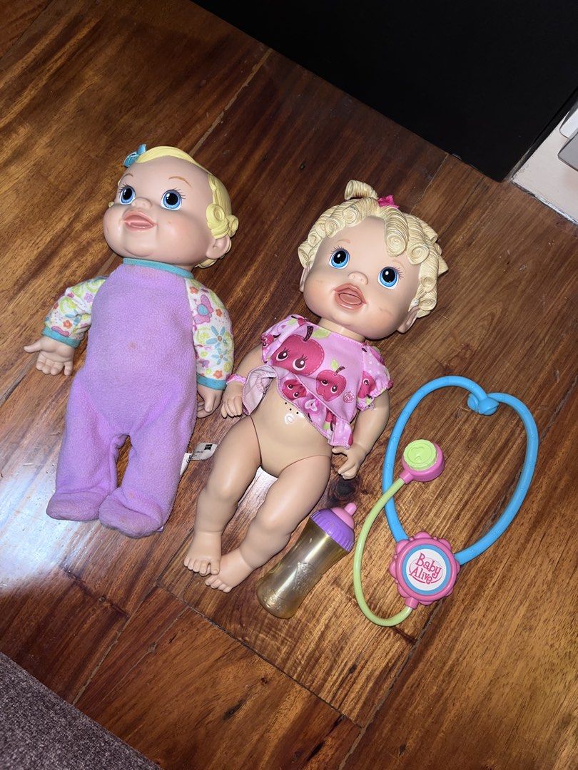 2 Baby Alive Dolls with Accessories (Category: Kids Toys) located in Manila. Submitted by oogbe (Listing ID 1460364802, Image 2). Description: - Set of two Baby Alive dolls - One doll in purple romper (minor marks on romper) - Second doll in pink apple-themed shirt - Includes baby bottle - Includes toy stethoscope - Perfect for pretend play - Selling as a set.
