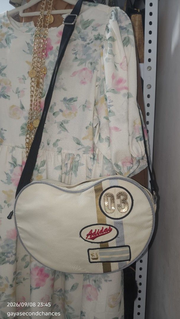 A DIDAS HEART SHAPE SLING BAG (Category: Shoulder Bags) located in Kalibo. Submitted by secondchances.thriftsh8p (Listing ID 1460480939, Image 3). Description: - Cute cream heart-shaped shoulder bag from Adidas. - Features iconic Adidas logo. - Adorned with a sequined '03' patch. - Adjustable strap for comfortable wear. - Versatile for everyday use or as a stylish accessory. - Unique and eye-catching design..
