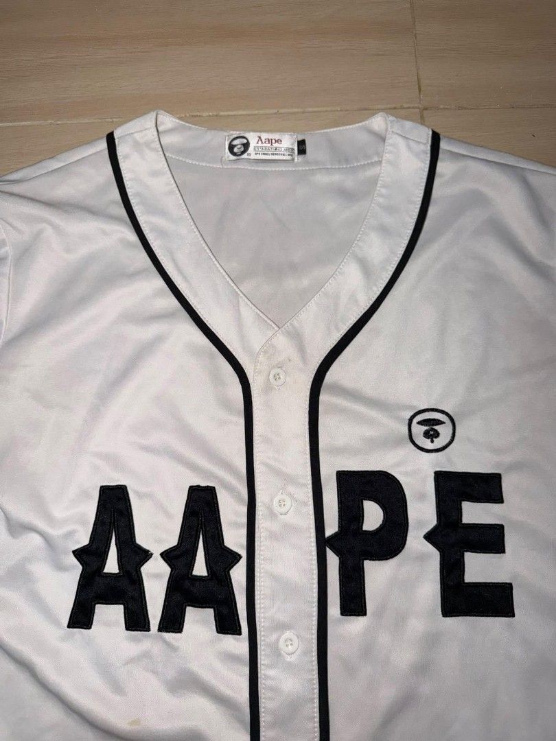 AAPE BY A BATHING APE White Baseball Jersey (Category: Tshirts & Polo Shirts ) located in Cainta. Submitted by hermosooo (Listing ID 1460432708, Image 2). Description: - White AAPE baseball jersey - Black trim and lettering - AAPE logo on chest and sleeve - Button-up front - Ideal for casual or streetwear outfits.