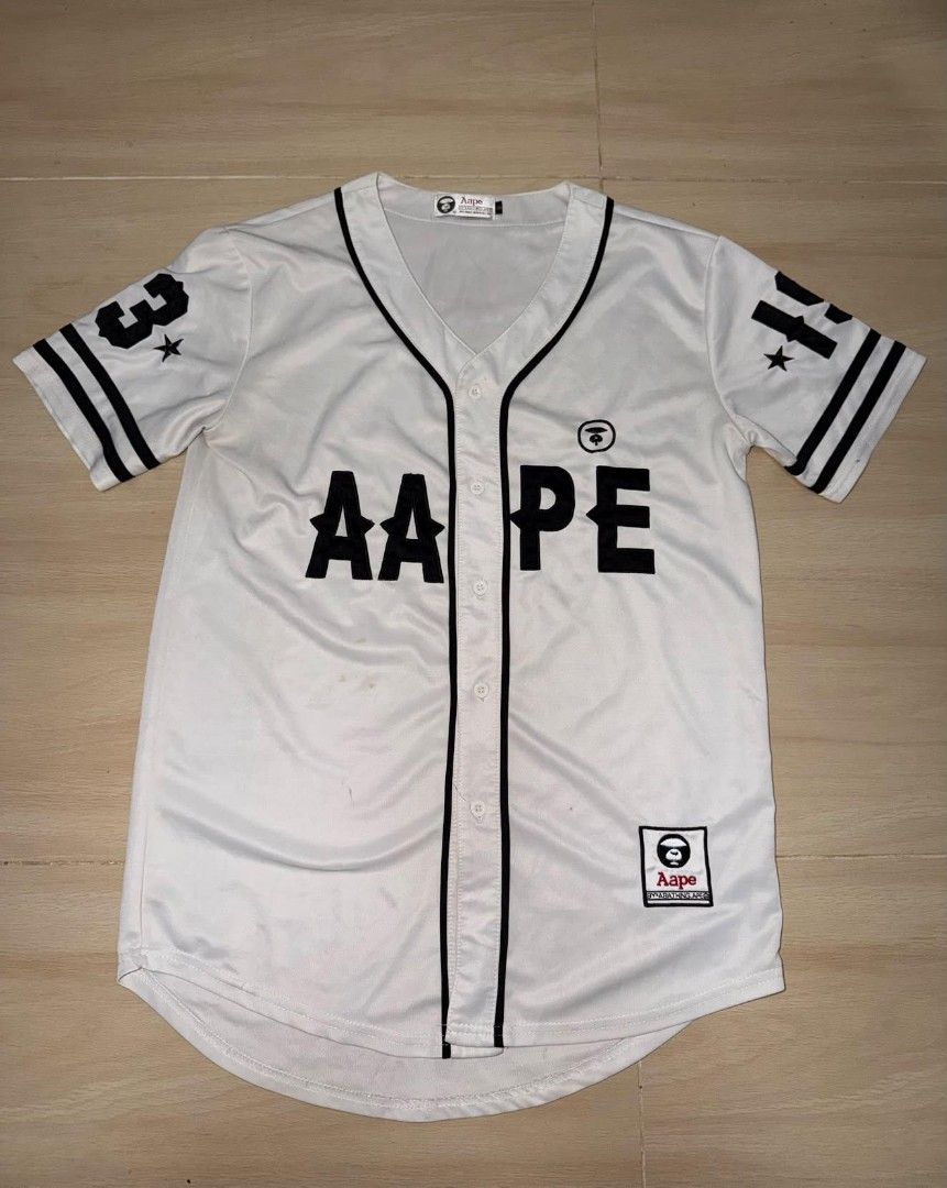 AAPE BY A BATHING APE White Baseball Jersey (Category: Tshirts & Polo Shirts ) located in Cainta. Submitted by hermosooo (Listing ID 1460432708, Image 1). Description: - White AAPE baseball jersey - Black trim and lettering - AAPE logo on chest and sleeve - Button-up front - Ideal for casual or streetwear outfits.