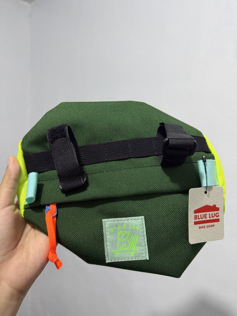 BLUE LUG Handlebar Bag [BNEW] (Category: Bicycles) located in Pulilan. Submitted by __ri__ (Listing ID 1460456465, Image 2). Description: - Green handlebar bag from BLUE LUG Bike Shop - Bright yellow accents on the sides - Features velcro straps for secure mounting - Includes a small patch with a cute cat graphic - Orange zipper pull for easy access - Ideal for carrying essentials on your bike rides - BRAND NEW.