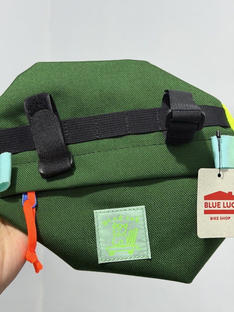 BLUE LUG Handlebar Bag [BNEW] (Category: Bicycles) located in Pulilan. Submitted by __ri__ (Listing ID 1460456465, Image 1). Description: - Green handlebar bag from BLUE LUG Bike Shop - Bright yellow accents on the sides - Features velcro straps for secure mounting - Includes a small patch with a cute cat graphic - Orange zipper pull for easy access - Ideal for carrying essentials on your bike rides - BRAND NEW.