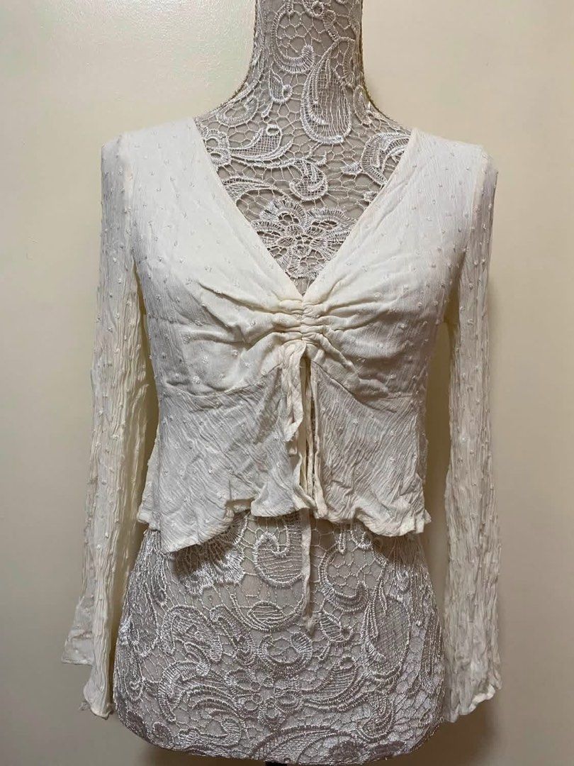 Cream White Ruched Front Tie Long Sleeve Top (Category: Blouses) located in Manila. Submitted by airamef28.closet (Listing ID 1460416921, Image 1). Description: - Cream white long sleeve top - Ruched tie front detail - V-neckline - Open back with button closure and tie detail - Bell sleeves - Textured fabric with subtle dots - Estimated size S/M - Ideal for boho or casual outfits.