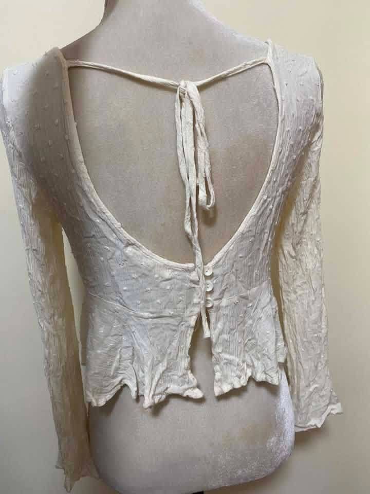 Cream White Ruched Front Tie Long Sleeve Top (Category: Blouses) located in Manila. Submitted by airamef28.closet (Listing ID 1460416921, Image 2). Description: - Cream white long sleeve top - Ruched tie front detail - V-neckline - Open back with button closure and tie detail - Bell sleeves - Textured fabric with subtle dots - Estimated size S/M - Ideal for boho or casual outfits.