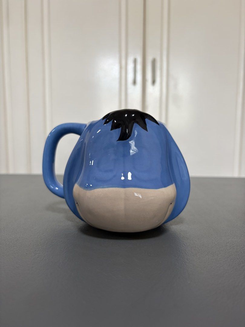 Eeyore Ceramic Mug (Category: Coffee & Tea Tableware) located in Paranaque City. Submitted by mayan_q (Listing ID 1460355506, Image 1). Description: - Adorable Eeyore mug with his classic sad expression. - Made of durable blue ceramic. - Ideal for your morning coffee or tea. - A must-have for any Winnie the Pooh enthusiast. - Adds a touch of fun to your kitchenware. - Dishwasher and microwave safe for convenience. - Approximately 4 inches tall. R
