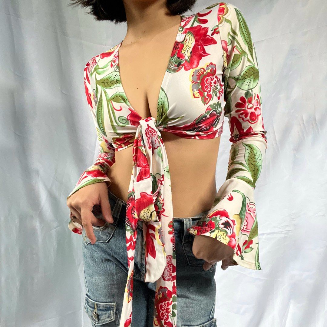 Floral Tie Front Long Sleeve Crop Top (Category: Blouses) located in Manila. Submitted by demi.rewears (Listing ID 1460314742, Image 2). Description: Chic white crop top with a vibrant red & green floral print. Features a deep V-neck, tie front, and long bell sleeves for a retro look. Perfect with high-waisted bottoms! Size: Fits XS to Small Bust: Fits 28” to 31” (14.3” flat lay) Length: 11”.