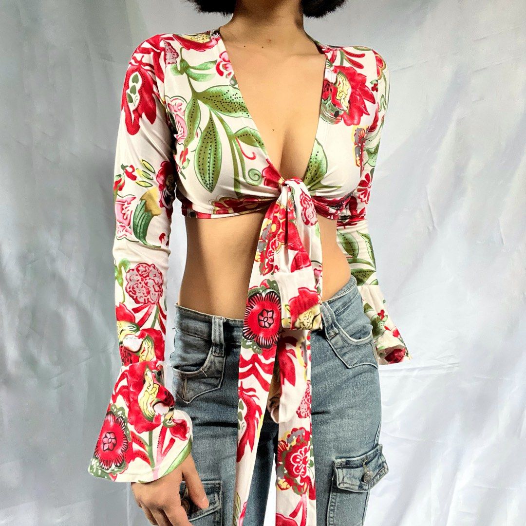 Floral Tie Front Long Sleeve Crop Top (Category: Blouses) located in Manila. Submitted by demi.rewears (Listing ID 1460314742, Image 3). Description: Chic white crop top with a vibrant red & green floral print. Features a deep V-neck, tie front, and long bell sleeves for a retro look. Perfect with high-waisted bottoms! Size: Fits XS to Small Bust: Fits 28” to 31” (14.3” flat lay) Length: 11”.