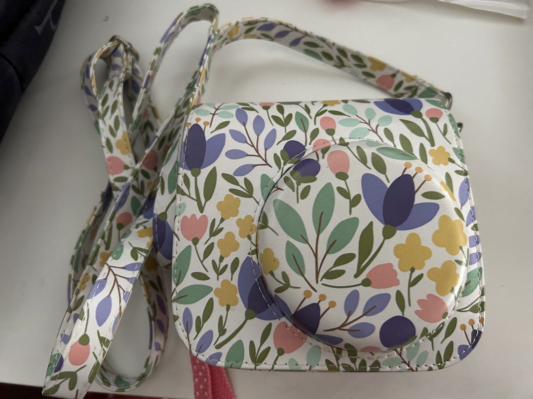 Instax Floral Camera Case with Strap (Category: Camera Bags & Carriers) located in Quezon City. Submitted by petrichorshop_ (Listing ID 1460327755, Image 1). Description: - Adorable floral print camera case - Includes a matching adjustable strap - Provides stylish protection for your camera - Fits instant cameras like Instax Mini - Features a white background with purple, pink, and yellow flowers and green leaves - A perfect accessory to personal