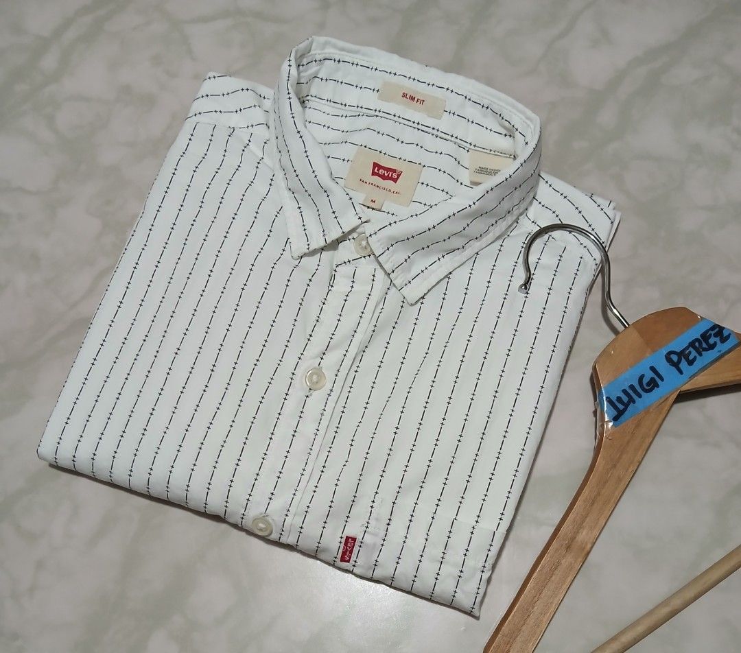 Levi's Slim Fit Striped Button-Up Shirt Medium (Category: Tshirts & Polo Shirts ) located in Plaridel. Submitted by igieperez147282 (Listing ID 1460343564, Image 3). Description: - White Levi's shirt with thin dark stripes - Slim fit style - Size: Medium - Measurements: 20" pit to pit, 27" length - Button-up front with a chest pocket - Classic Levi's red tab detail - Versatile for casual or smart casual outfits.