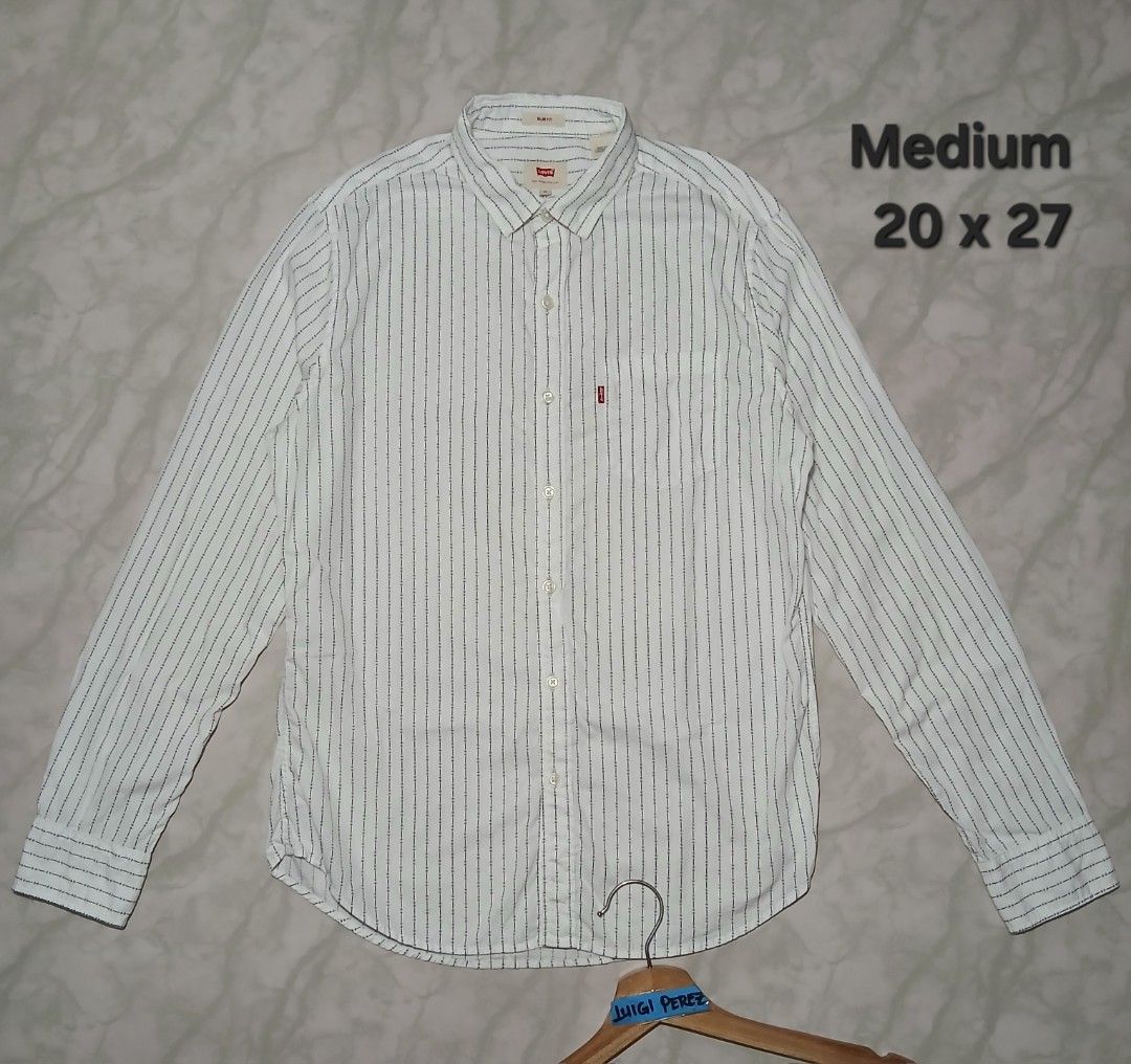 Levi's Slim Fit Striped Button-Up Shirt Medium (Category: Tshirts & Polo Shirts ) located in Plaridel. Submitted by igieperez147282 (Listing ID 1460343564, Image 1). Description: - White Levi's shirt with thin dark stripes - Slim fit style - Size: Medium - Measurements: 20" pit to pit, 27" length - Button-up front with a chest pocket - Classic Levi's red tab detail - Versatile for casual or smart casual outfits.