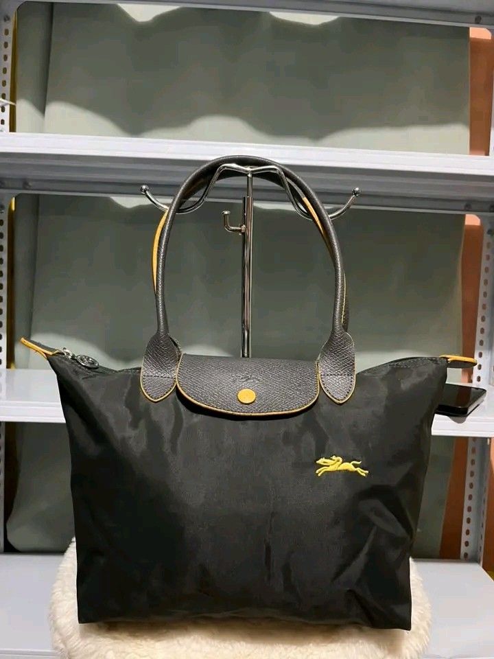 Longchamp Le Pliage Neo Tote Bag (Category: Luxury Bags & Wallets) located in Carmen. Submitted by ar_thrift00 (Listing ID 1460457082, Image 1). Description: - Classic Longchamp tote bag - Color: Black nylon with grey leather trim and yellow accents - Iconic embroidered yellow horse logo - Closure: Zip with snap tab - Ideal for everyday use, travel, or work - Spacious interior - Comfortable handles.