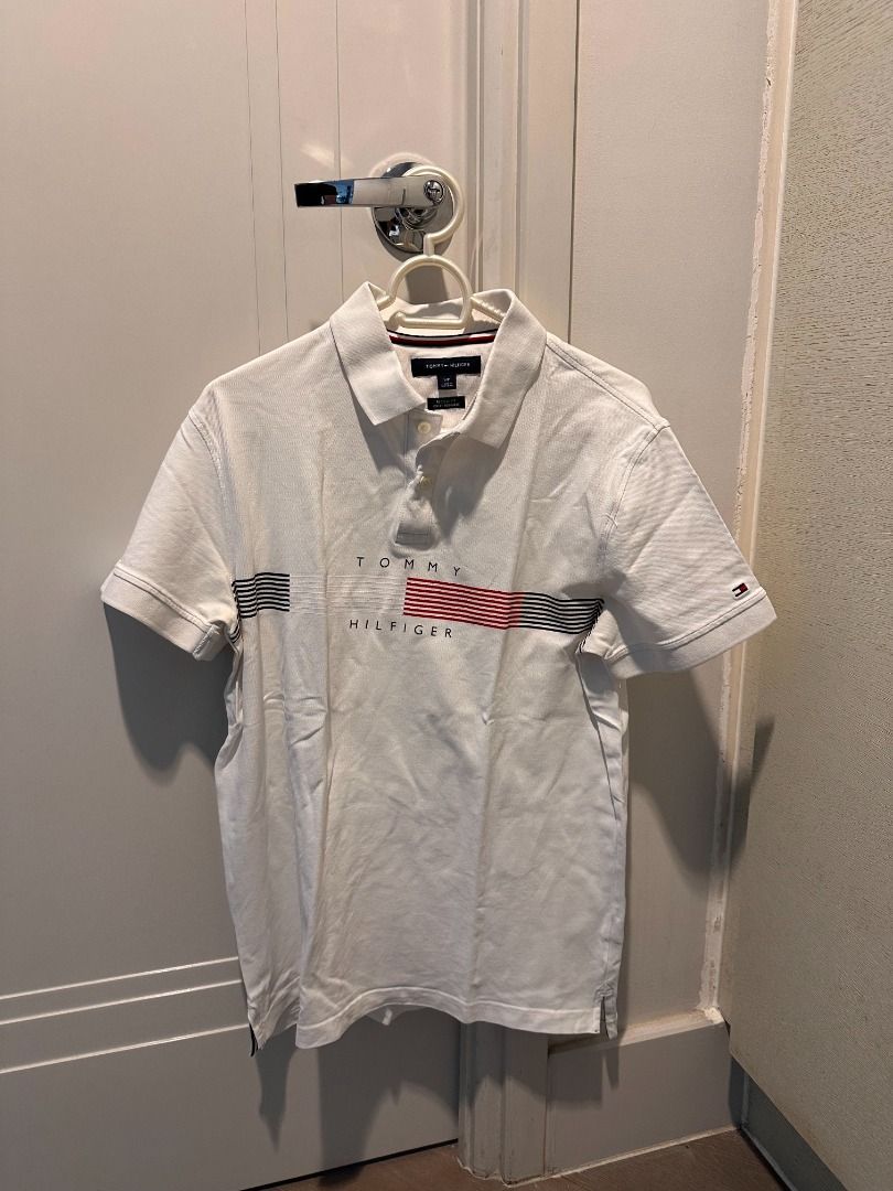 Tommy Hilfiger White Polo Shirt (Category: Tshirts & Polo Shirts ) located in Caloocan City. Submitted by jairustalu37822 (Listing ID 1460373886, Image 1). Description: - Classic white Tommy Hilfiger polo shirt - Features iconic Tommy Hilfiger logo on chest - Red and blue stripe detailing on collar/logo area - Short sleeves - Button-up collar - Ideal for everyday casual wear.