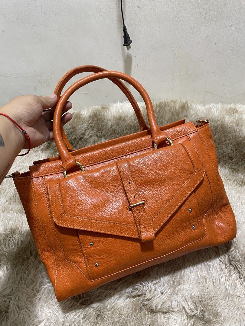 Tory Burch Orange Leather Tote Bag (Category: Shoulder Bags) located in Santiago. Submitted by UkayLuxxSelector (Listing ID 1460400747, Image 1). Description: - Stylish orange leather tote bag - Elegant gold hardware accents - Convenient front flap pocket with buckle closure - Practical zippered side pocket - Studded bottom for added protection and durability - Generously spacious interior - Ideal for everyday use and errands.